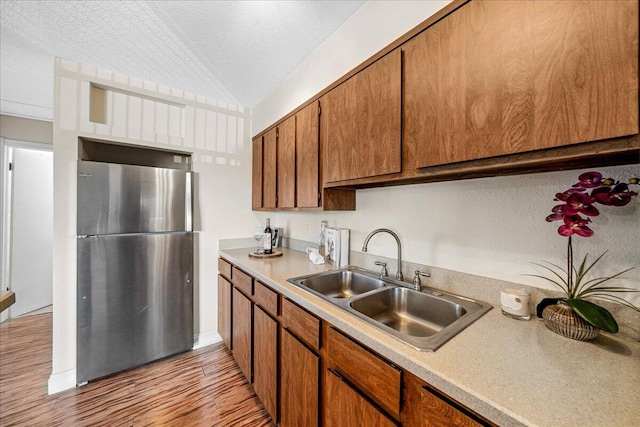 kitchen featuring stainless steel fridge, sink, light hardwood / wood-style flooring, a textured ceiling, and lofted ceiling