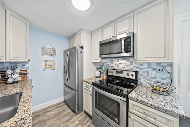 kitchen with light stone countertops, appliances with stainless steel finishes, decorative backsplash, and white cabinetry