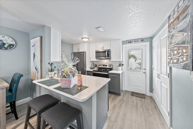 kitchen featuring a kitchen breakfast bar, light wood-type flooring, backsplash, gray cabinetry, and stainless steel appliances