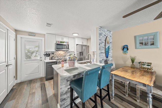 kitchen with white cabinets, appliances with stainless steel finishes, tasteful backsplash, a kitchen bar, and wood-type flooring