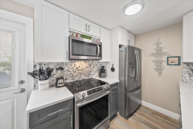 kitchen featuring white cabinetry, light stone counters, light hardwood / wood-style flooring, backsplash, and appliances with stainless steel finishes