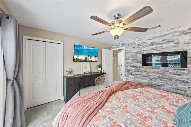 bedroom with ceiling fan, a textured ceiling, light carpet, and a closet