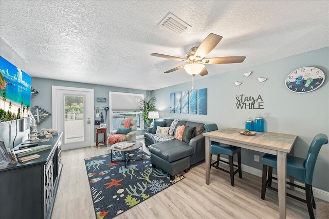 living room featuring ceiling fan, light hardwood / wood-style floors, and a textured ceiling