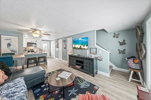 living room with a textured ceiling, light hardwood / wood-style floors, and ceiling fan