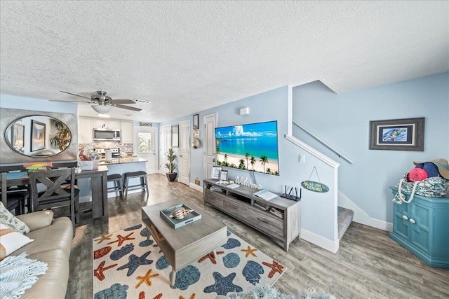 living room with ceiling fan, light wood-type flooring, and a textured ceiling