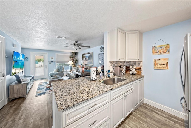 kitchen with backsplash, stainless steel refrigerator, sink, and white cabinets