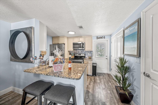 kitchen with dark wood-type flooring, dark stone counters, decorative backsplash, a breakfast bar, and appliances with stainless steel finishes