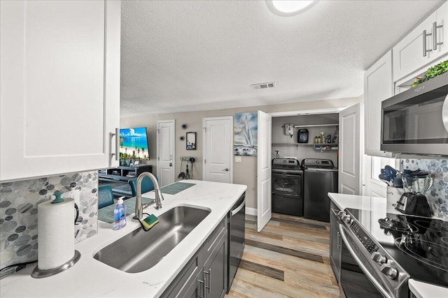 kitchen with appliances with stainless steel finishes, light wood-type flooring, sink, washing machine and clothes dryer, and white cabinets