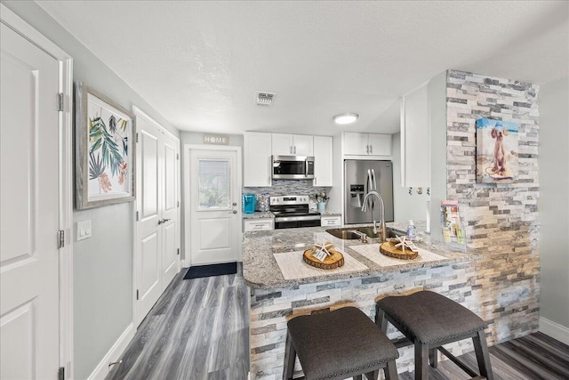 kitchen with kitchen peninsula, light stone counters, stainless steel appliances, sink, and white cabinetry