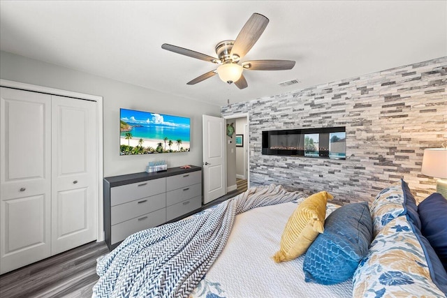 bedroom with a tile fireplace, ceiling fan, a closet, and wood-type flooring