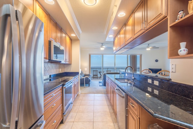 kitchen with stainless steel appliances, ceiling fan, dark stone countertops, and sink