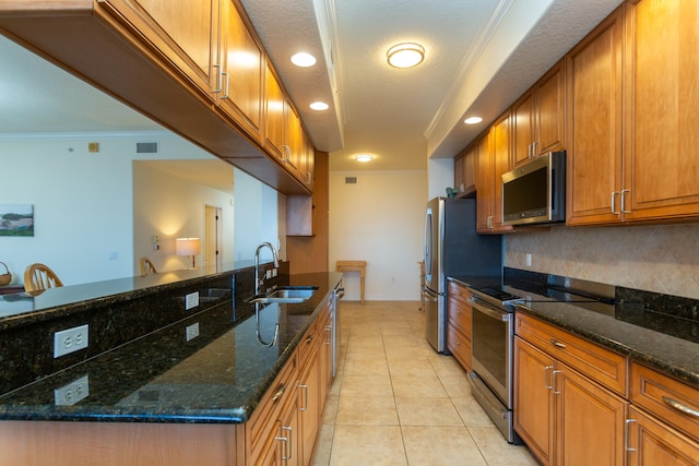 kitchen with sink, light tile floors, ornamental molding, appliances with stainless steel finishes, and dark stone countertops