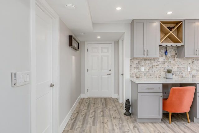 bar with backsplash, gray cabinetry, light hardwood / wood-style flooring, and built in desk