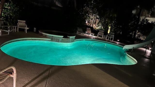 pool at twilight featuring an in ground hot tub, a water slide, and a patio area