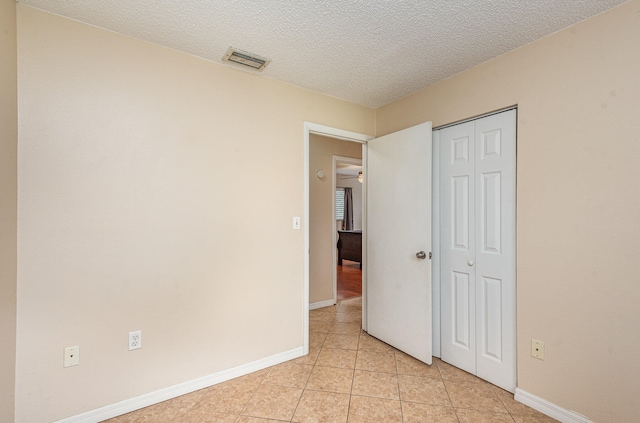 unfurnished bedroom featuring light tile floors, a textured ceiling, and a closet