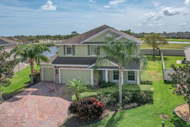 view of front of property featuring an attached garage, fence, decorative driveway, stucco siding, and a front lawn