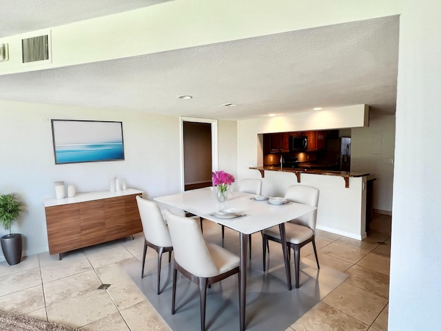 dining area featuring light tile patterned floors, baseboards, visible vents, and a textured ceiling