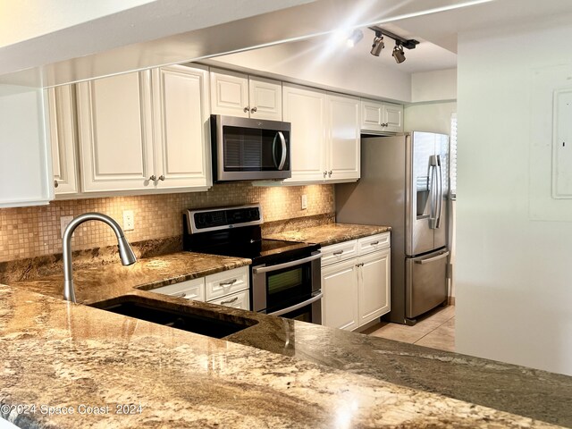 kitchen with tasteful backsplash, stainless steel appliances, stone counters, white cabinetry, and a sink