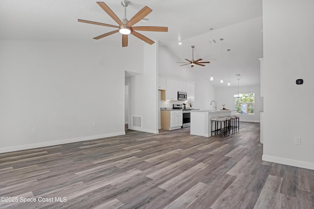 unfurnished living room featuring ceiling fan with notable chandelier, a sink, wood finished floors, visible vents, and baseboards