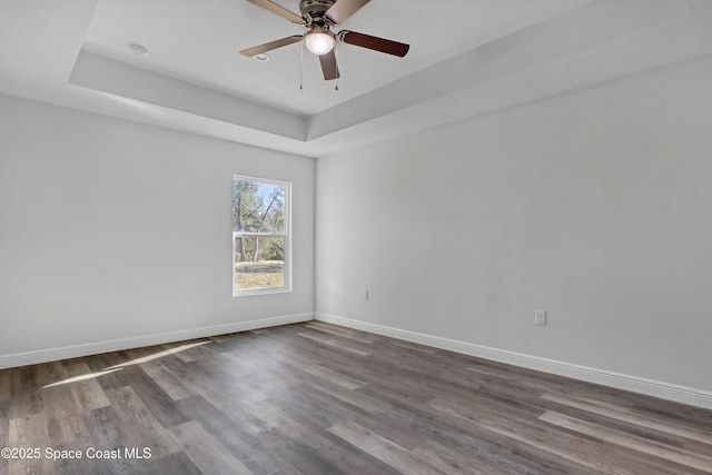 empty room with a ceiling fan, baseboards, a tray ceiling, and dark wood-style flooring