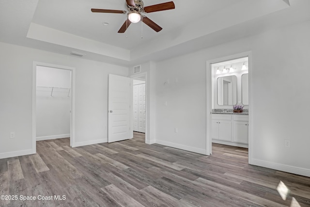 unfurnished bedroom featuring a raised ceiling, visible vents, baseboards, and wood finished floors