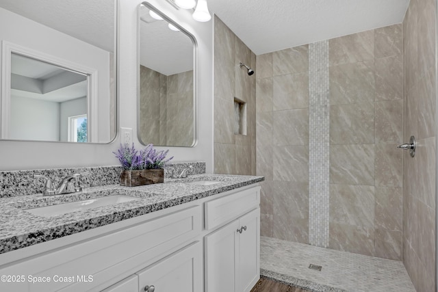 full bath with double vanity, a textured ceiling, a sink, and tiled shower