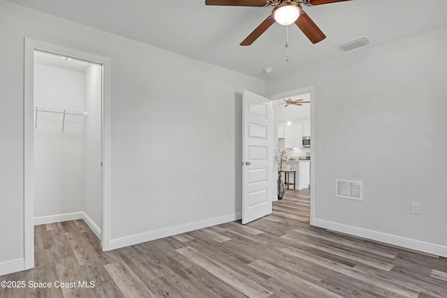 unfurnished room with ceiling fan, wood finished floors, visible vents, and baseboards