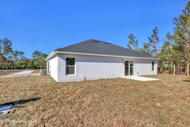 back of property with roof with shingles, central AC unit, a lawn, and stucco siding