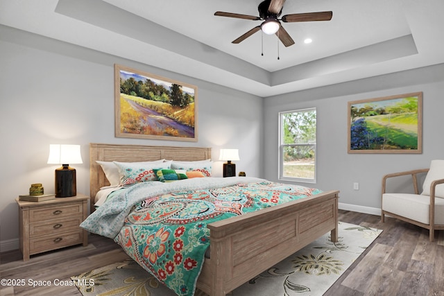 bedroom with a ceiling fan, a raised ceiling, baseboards, and wood finished floors