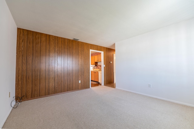 unfurnished room featuring wood walls and light carpet