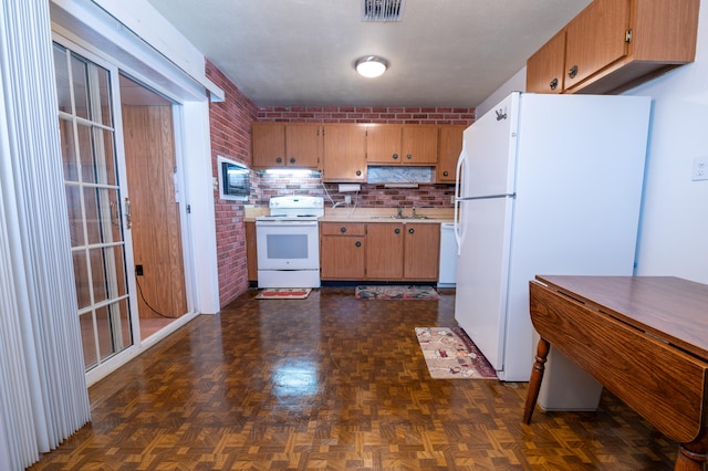 kitchen featuring dark parquet flooring, sink, brick wall, white appliances, and decorative backsplash