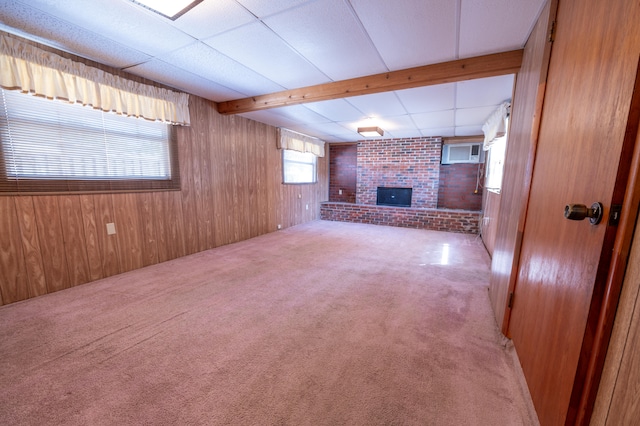 unfurnished living room with a brick fireplace, brick wall, light colored carpet, beam ceiling, and wood walls