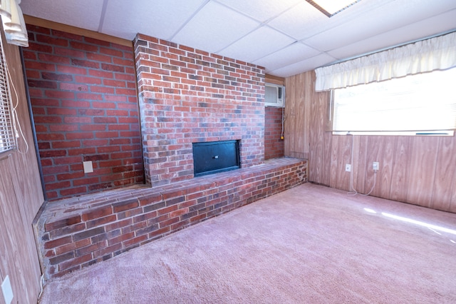 unfurnished living room featuring an AC wall unit, a paneled ceiling, wooden walls, and light carpet