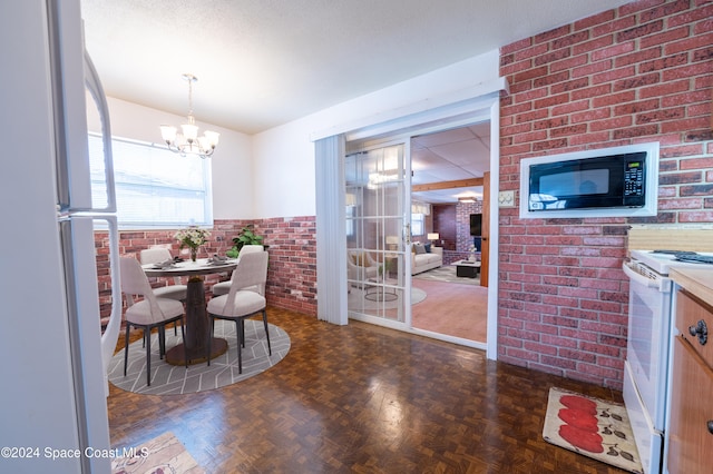 dining area featuring dark parquet floors, a notable chandelier, and brick wall