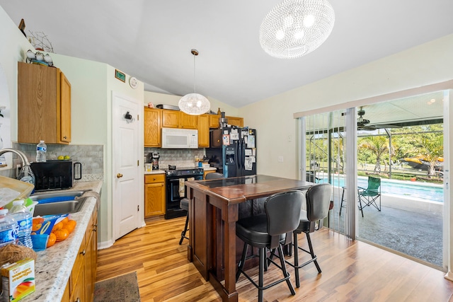 kitchen featuring decorative light fixtures, black appliances, light hardwood / wood-style flooring, vaulted ceiling, and tasteful backsplash