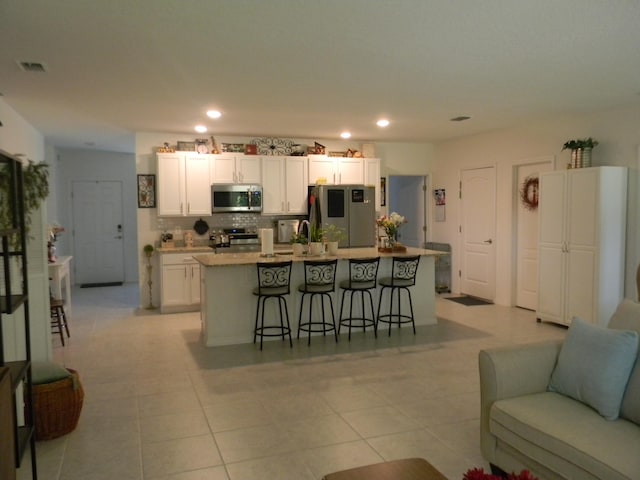 kitchen featuring appliances with stainless steel finishes, a breakfast bar, an island with sink, light tile floors, and white cabinets