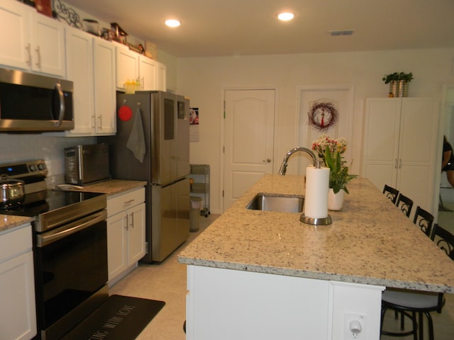 kitchen with light tile floors, a center island with sink, a breakfast bar area, and stainless steel appliances