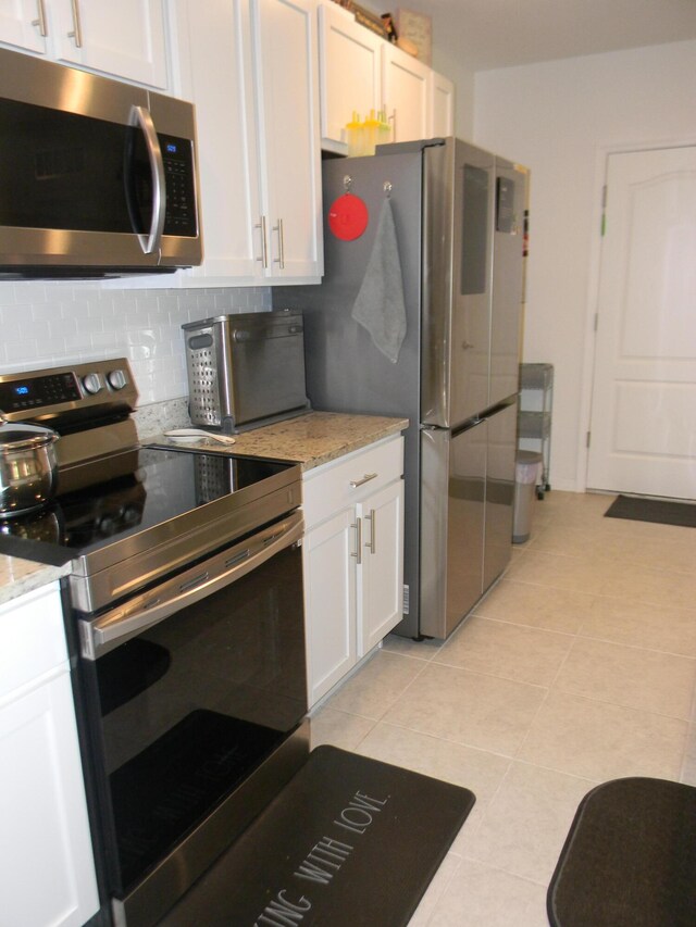 kitchen featuring white cabinetry, backsplash, light tile flooring, appliances with stainless steel finishes, and light stone counters