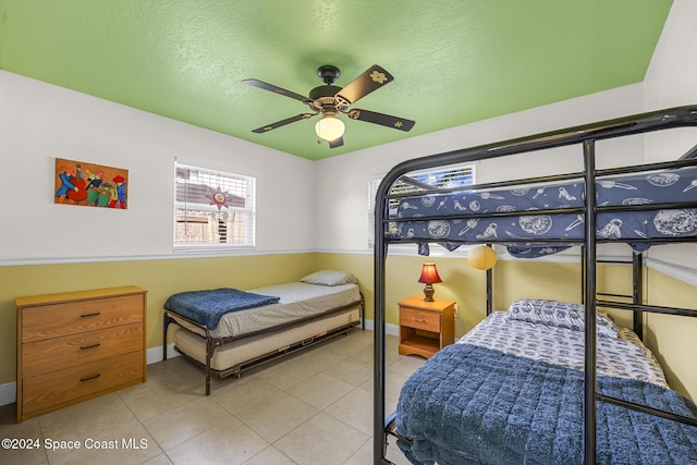 bedroom featuring ceiling fan, light tile patterned floors, and a textured ceiling