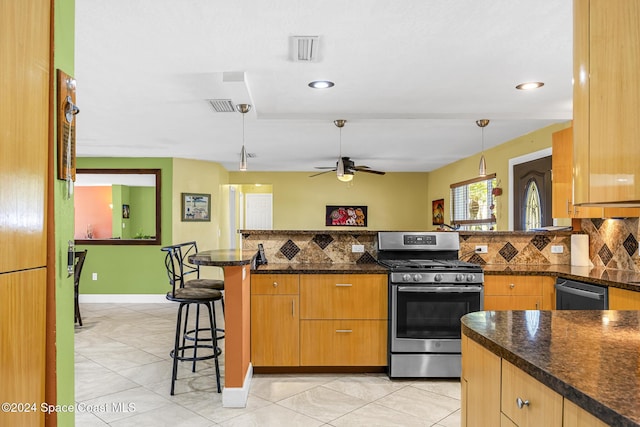 kitchen featuring pendant lighting, ceiling fan, dark stone countertops, a kitchen bar, and stainless steel appliances