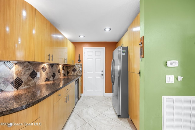 kitchen with light tile patterned flooring, appliances with stainless steel finishes, tasteful backsplash, and dark stone countertops