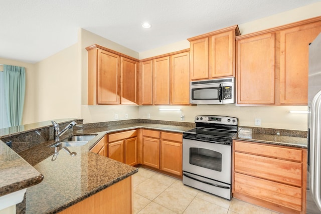 kitchen featuring appliances with stainless steel finishes, dark stone counters, sink, and light tile flooring