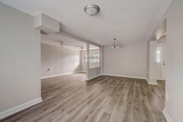 unfurnished room with a textured ceiling, ceiling fan with notable chandelier, and dark wood-type flooring