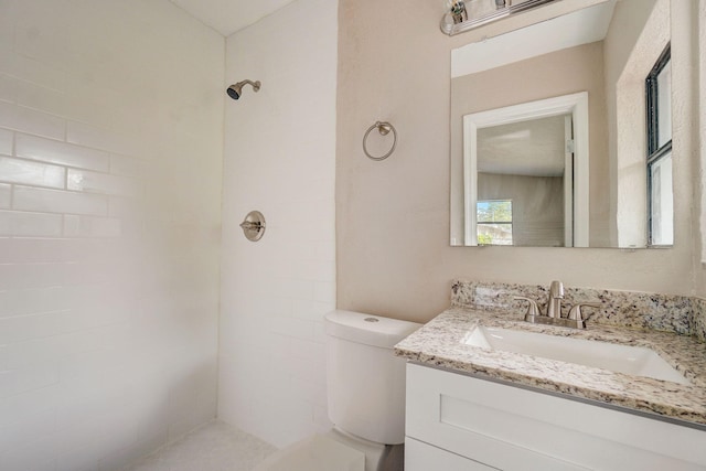 bathroom with toilet, a tile shower, and vanity with extensive cabinet space