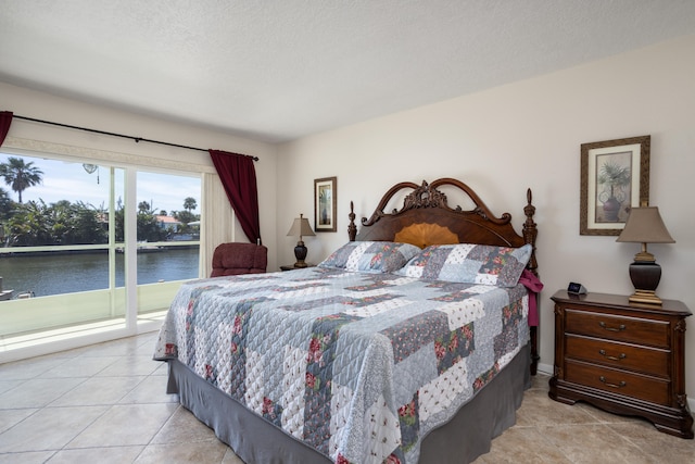 bedroom featuring light tile flooring, a water view, access to outside, and a textured ceiling