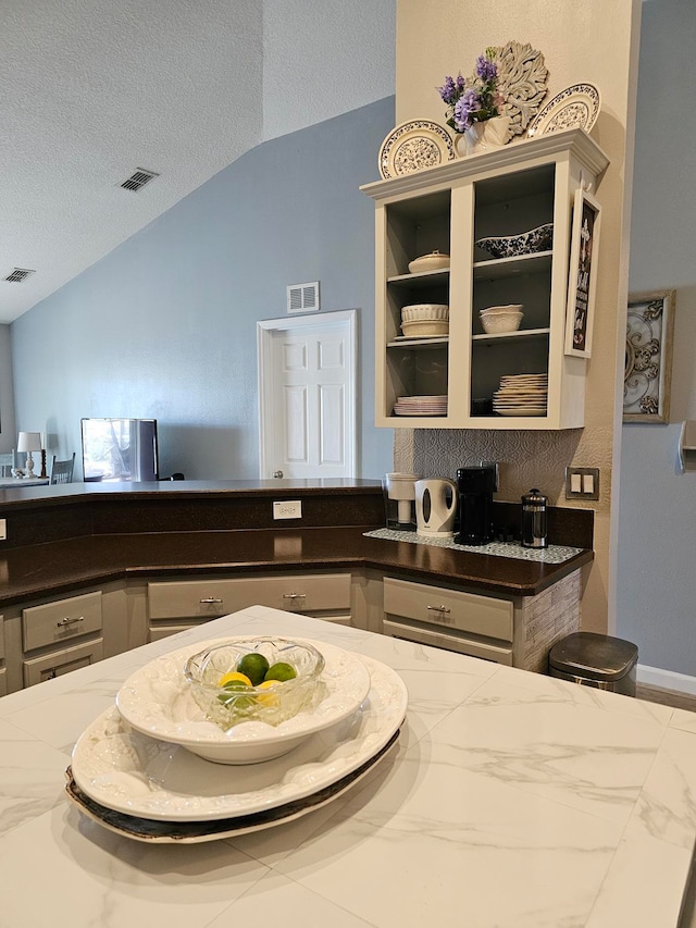 kitchen featuring a textured ceiling, white cabinets, dark stone countertops, and lofted ceiling