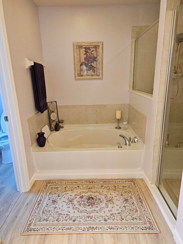 bathroom with hardwood / wood-style floors, shower with separate bathtub, and toilet