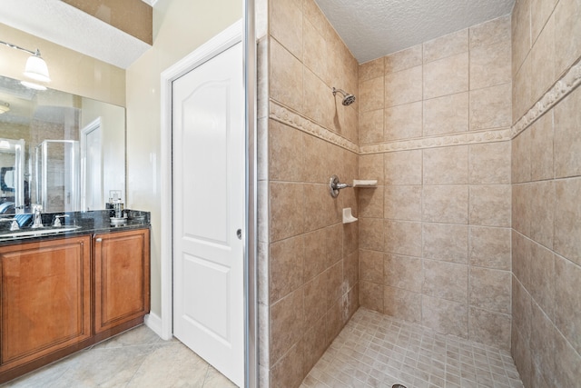 bathroom featuring tile flooring, vanity, a tile shower, and a textured ceiling