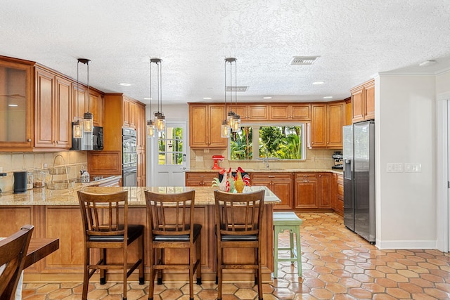 kitchen featuring a healthy amount of sunlight, stainless steel fridge, pendant lighting, and a kitchen breakfast bar