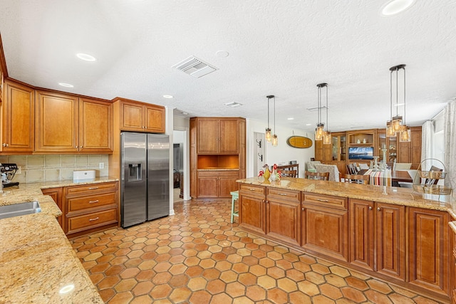 kitchen with decorative light fixtures, light tile flooring, stainless steel fridge, and light stone countertops